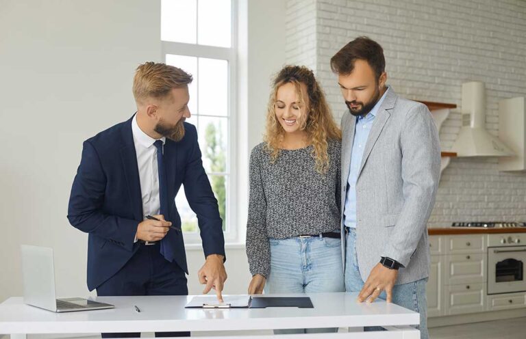 Two people sitting at a table reviewing home documents and discussing with a real estate agent.